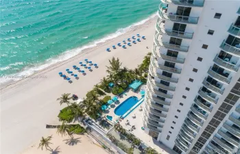 High-rise residential building featuring expansive private balconies, a ground-level swimming pool, integrated hardscaping, and immediate coastal access