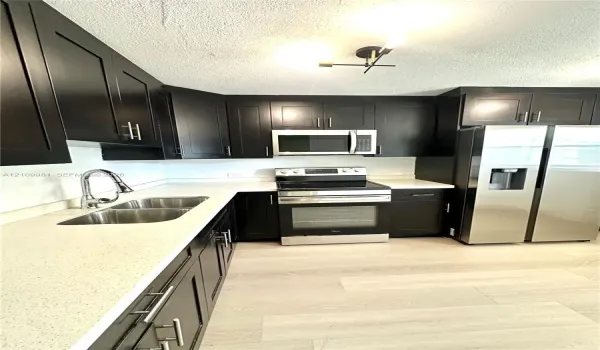 Kitchen featuring dark cabinetry, stone-finish countertops, stainless steel appliances, a double-basin undermount sink with a gooseneck faucet, and wood-finish flooring