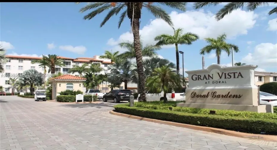 Gran Vista at Doral community entrance featuring a masonry signage monument, paver stone driveways, mature palm trees, and manicured landscaping