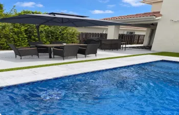 Backyard area featuring a swimming pool with stone coping, artificial turf border, concrete patio, and a covered lanai