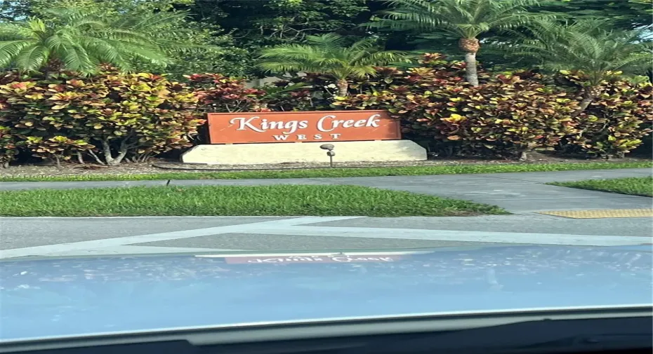 Community signage featuring structural masonry base and mature tropical landscaping including palm trees and croton shrubs