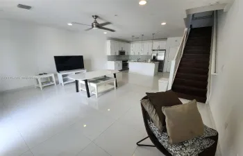 Open-concept interior featuring large-format tile flooring, white cabinetry, a kitchen island, recessed lighting, and a staircase with dark wood-finish treads