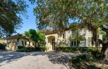 Stucco exterior featuring an arched entryway, tile roof, multi-car garage, upper-level balcony with metal railing, and paver driveway