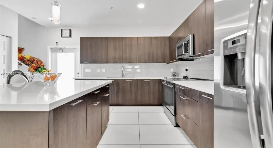 Kitchen featuring flat-panel wood-finish cabinetry, white countertops, stainless steel appliances, subway tile backsplash, and large-format floor tile