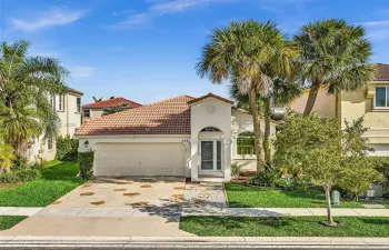 Stucco exterior featuring a tiled roof, arched entryway, attached two-car garage, and decorative stone-accented driveway