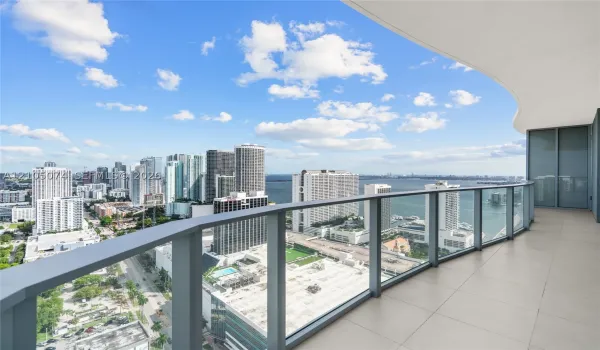 Spacious private balcony with large-format floor tiles and a curved structural design, featuring a glass-panel railing and extensive water and city skyline outlooks