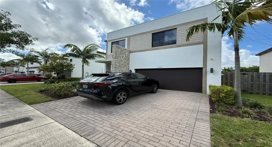 Modern two-story exterior featuring smooth stucco finish, horizontal siding accents, stone veneer detail, and a paver driveway leading to a multi-car garage