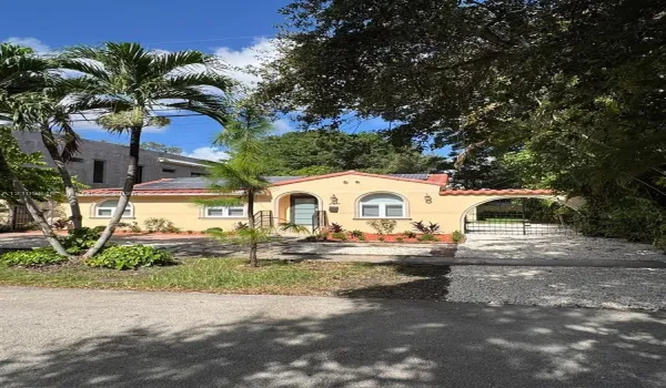 Single-story exterior featuring stucco siding, arched entryway, clay tile roof detailing, roof-mounted solar panels, and a decorative arched gate