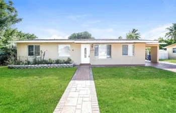 Single-story exterior featuring a concrete-tile walkway, stone-block landscaping border, and covered carport