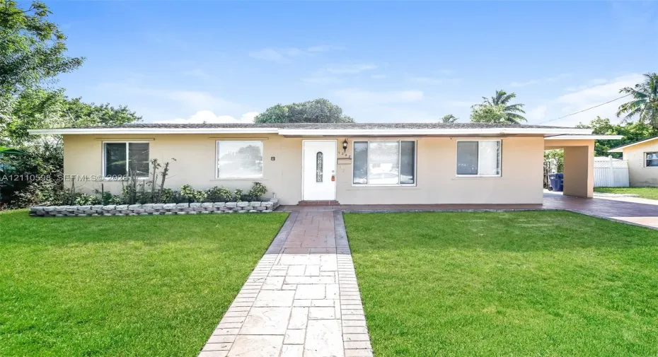 Single-story exterior featuring a concrete-tile walkway, stone-block landscaping border, and covered carport