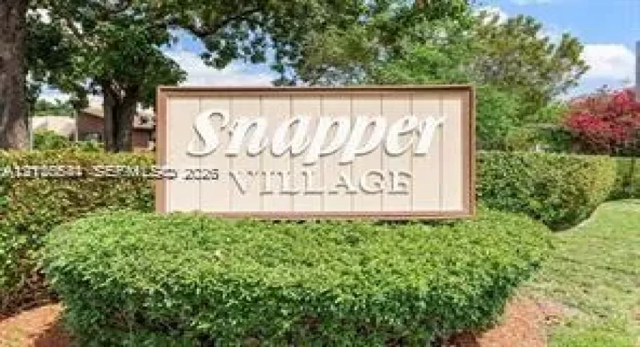 Community signage featuring a wood-frame monument with raised lettering, surrounded by manicured hedges and mature landscaping