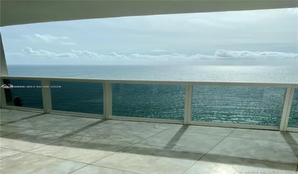 Covered balcony featuring large-format tile flooring and a glass-paneled railing overlooking the ocean