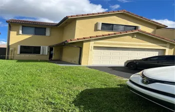 Two-story exterior featuring a stucco facade, red tile roof, attached two-car garage with a sectional door, and asphalt driveway