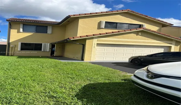 Two-story exterior featuring a stucco facade, red tile roof, attached two-car garage with a sectional door, and asphalt driveway