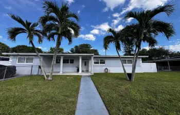 Single-story exterior featuring a covered entryway with decorative columns, a concrete walkway, and mature palm trees