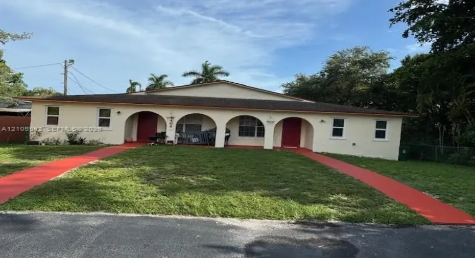 Duplex property featuring a stucco exterior, twin red entry doors, and arched porch details