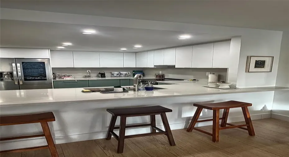 Kitchen featuring two-tone cabinetry, stainless steel refrigerator, stone-surface breakfast bar with integrated sink, recessed lighting, and wood-finish flooring