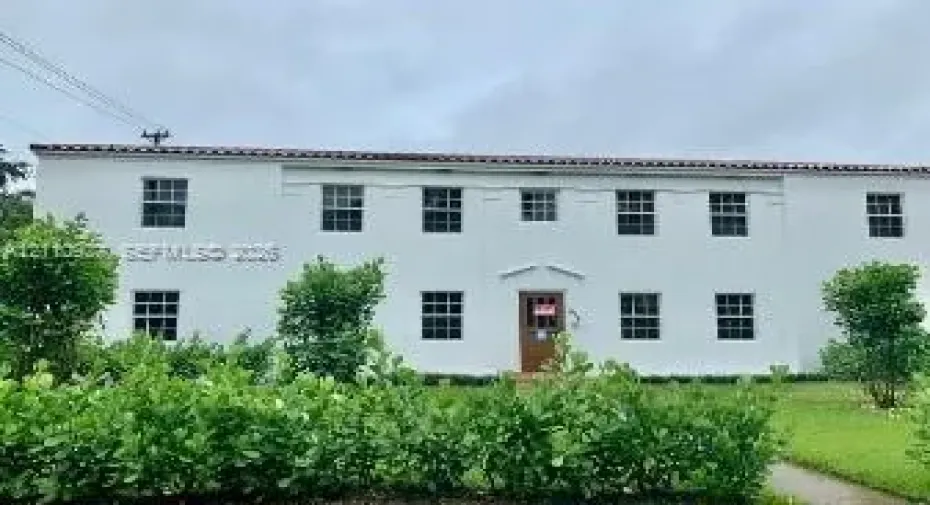 Two-story stucco exterior featuring a terra cotta tile roof, symmetrical window placement, and a centered entryway