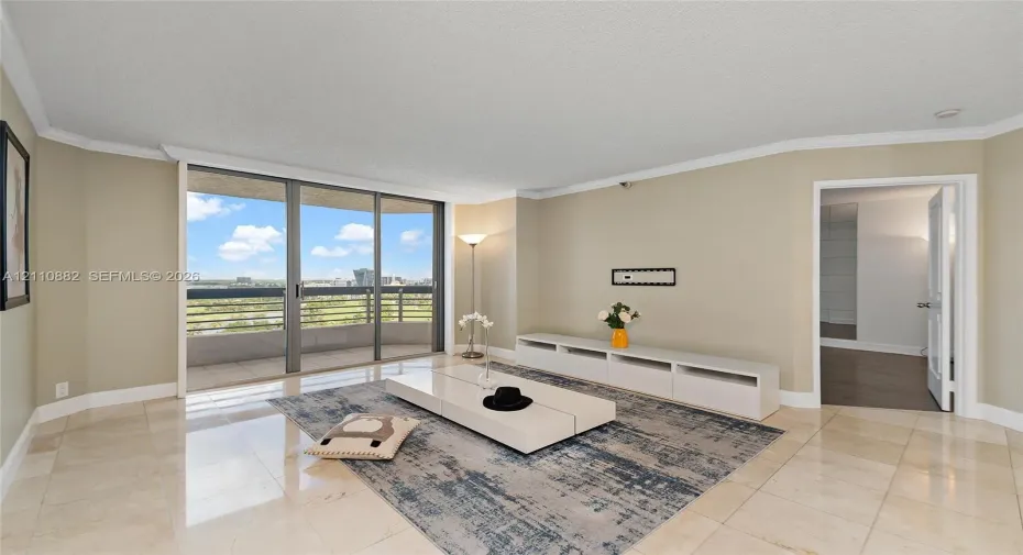 Living area featuring neutral stone flooring, crown molding, and floor-to-ceiling sliding glass doors opening to a private balcony