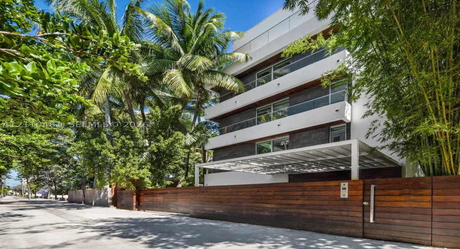 Multi-story contemporary exterior featuring horizontal wood siding, smooth white stucco facade, glass balcony railings, and a gated entrance with horizontal wood fencing