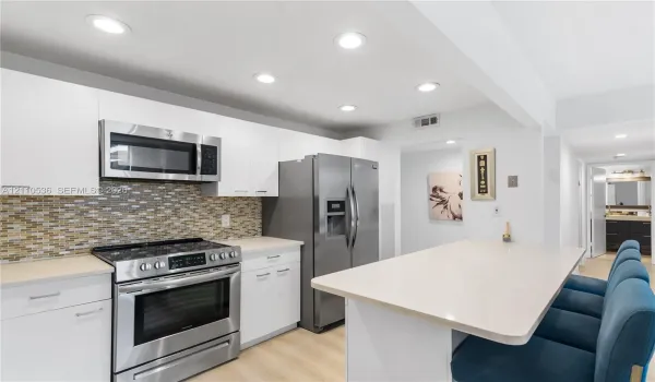 Kitchen featuring flat-panel white cabinetry, stainless steel appliances, multi-tonal glass tile backsplash, light-toned countertop, and recessed lighting