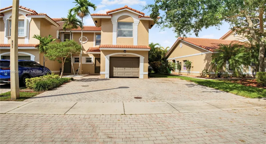 Stucco exterior with a tiled roof, attached garage, and paved driveway
