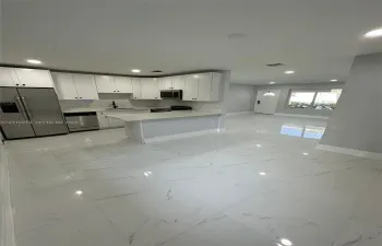 Kitchen featuring white shaker-style cabinetry, quartz countertops, a peninsula with bar seating, stainless steel appliances, and large-format porcelain tile flooring