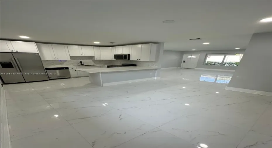 Kitchen featuring white shaker-style cabinetry, quartz countertops, a peninsula with bar seating, stainless steel appliances, and large-format porcelain tile flooring