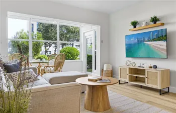 Living area featuring large windows with natural light, wood-finish flooring, and a wall-mounted floating shelf