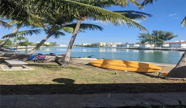 Waterfront exterior space featuring a concrete bulkhead, stone bench, and palm trees