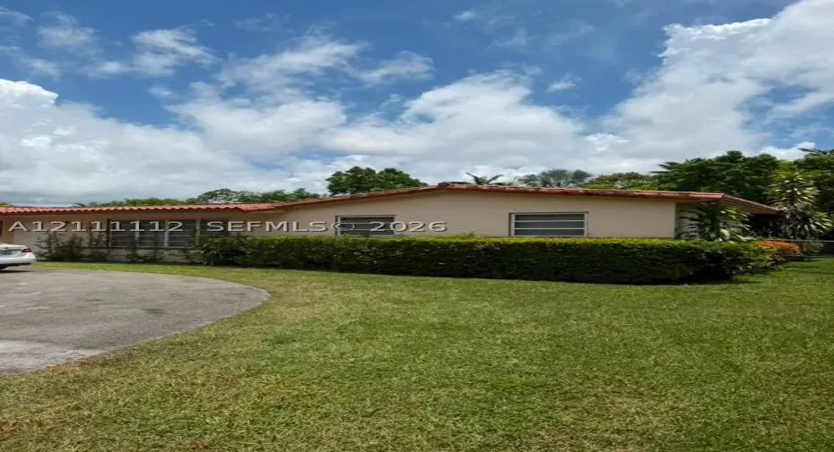 Single-story residence featuring a low-pitch tile roof, stucco exterior, expansive lawn, and concrete driveway