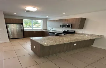 Kitchen featuring wood-finish cabinetry, stone-surface countertops, stainless steel appliances, a peninsula, and ceramic tile flooring