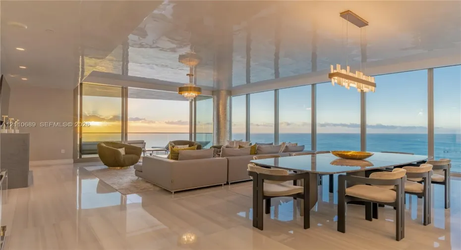 Open-concept interior featuring floor-to-ceiling glass walls, polished stone flooring, a reflective ceiling finish, and custom tiered and linear pendant lighting