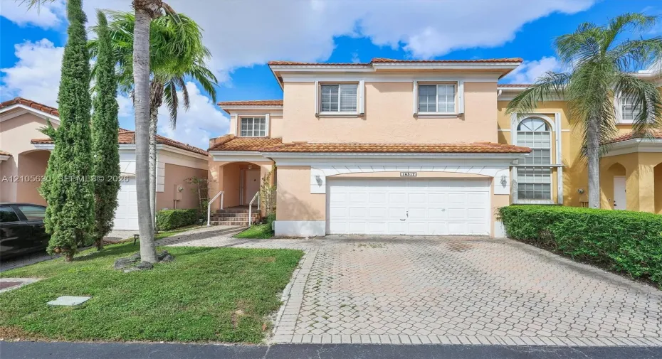 Two-story stucco exterior featuring a tile roof, an arched entryway, and an attached two-car garage with a paver driveway