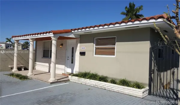 Single-story residence featuring a tile roof, covered front porch supported by classic columns, decorative brick-accented exterior, and a paved driveway