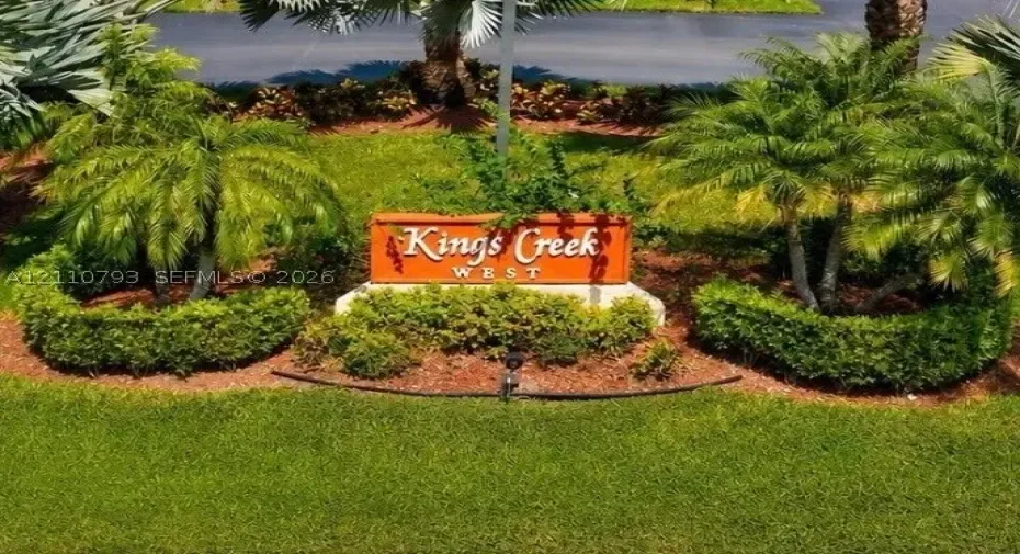 Community signage featuring raised lettering, surrounded by manicured shrubbery, mulch beds, and mature palm trees
