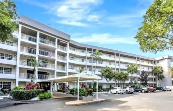 Multi-story residential building featuring covered porte-cochère entry, private balconies, and mature palm landscaping