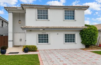 Two-story exterior featuring light-toned stucco, a concrete tile roof, double front entry doors, and a decorative paver driveway