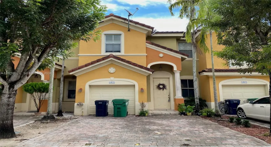 Stucco exterior featuring multi-toned facade, arched entryway with column accents, tile roof, and brick-paver driveway