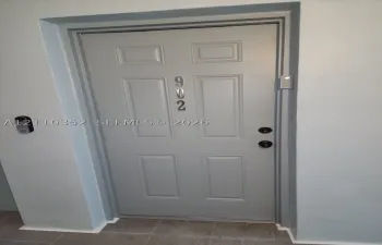 Six-panel entry door featuring a matte finish, metallic house numbering, dual-point locking hardware, and a mounted digital doorbell system