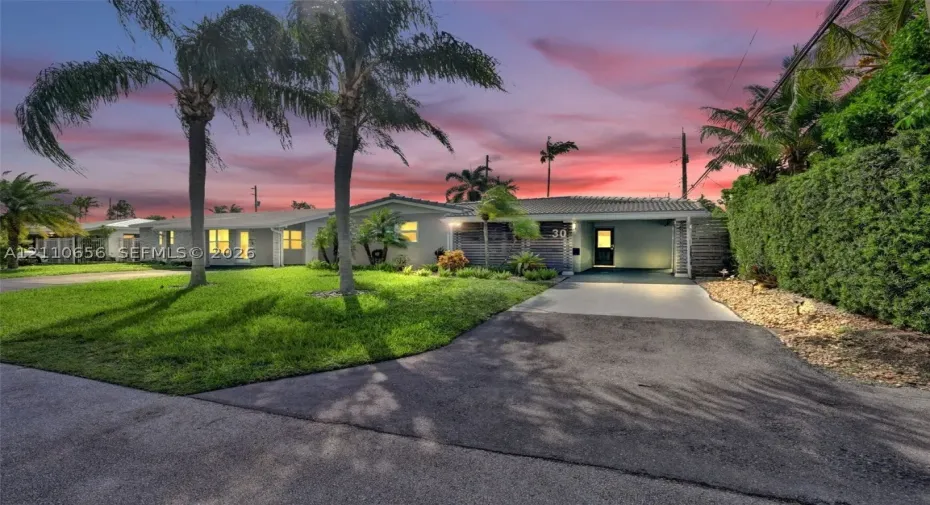 Single-story exterior featuring a concrete tile roof, integrated carport, manicured lawn, and established palm trees