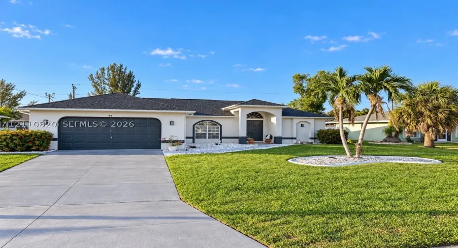Single-story exterior featuring a light-toned stucco façade, a dark multi-car garage, a covered entry with an arched transom window, a concrete driveway, and maintained landscape beds