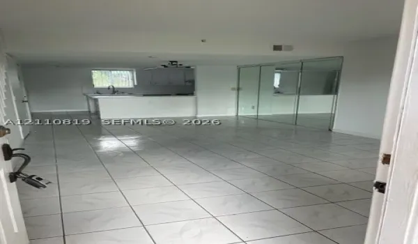 Open-concept interior featuring light-toned tile flooring, kitchen with peninsula, and wall-to-wall mirrored closet doors