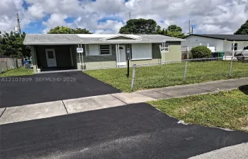 Single-story residence featuring a brick facade, covered carport, chain-link perimeter fencing, and an asphalt driveway
