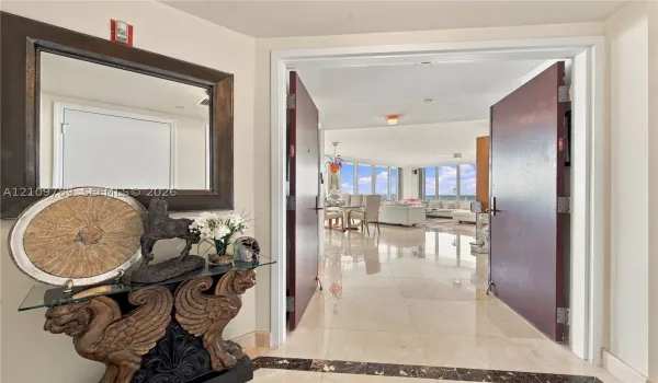 Foyer entrance featuring dual solid-core doors, polished stone flooring with a decorative dark stone inlay, and floor-to-ceiling windows