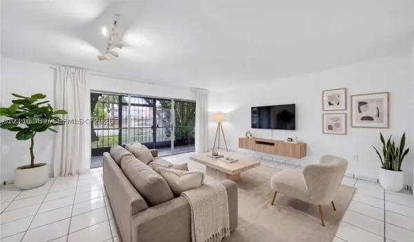 Spacious living area featuring large-format tile flooring, a wall-mounted wood-finish media console, track lighting, and expansive sliding glass doors