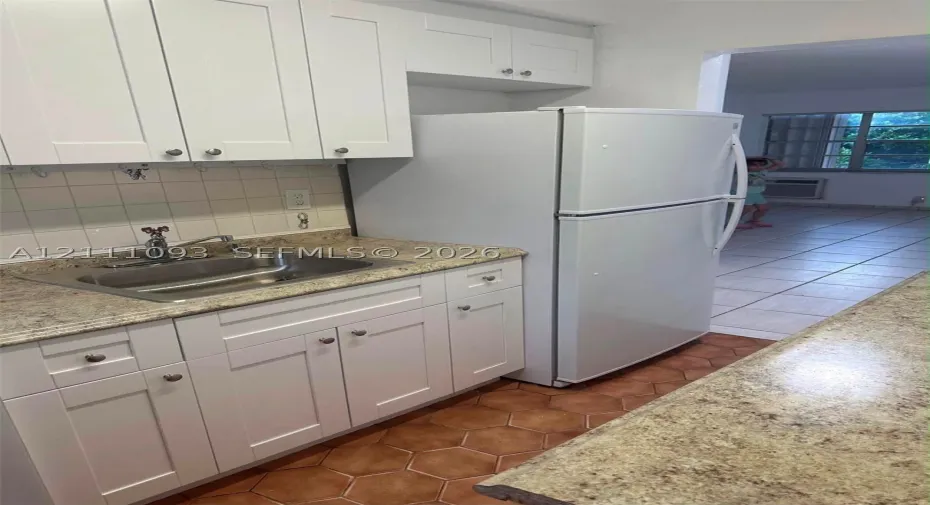 Kitchen featuring shaker-style white cabinetry, stone-finish countertops, stainless steel sink with metal faucet, and hexagonal ceramic tile flooring