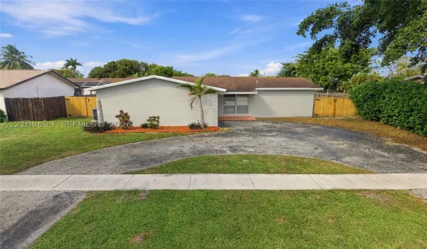 Single-story residence featuring a low-slope roof, textured exterior finish, circular paved driveway, and wood-panel fencing
