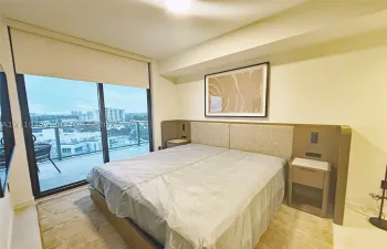 Floor-to-ceiling sliding glass door, built-in upholstered headboard, integrated bedside cabinetry, and private balcony with metal railing