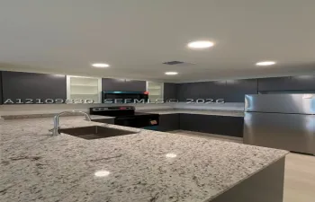 Kitchen featuring charcoal cabinetry with glass-panel accents, stone-composite countertops, stainless steel appliances, and a recessed undermount sink with a high-arch faucet